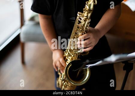 Vue rognée du garçon s'exerçant pour jouer au saxophone à accueil Banque D'Images