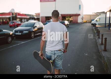 Jeune homme avec skateboard marchant sur la route en ville Banque D'Images