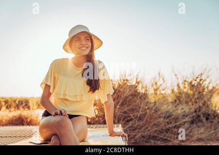 Jeune femme attentionnés assise sur un mur de soutènement contre un ciel dégagé au coucher du soleil Banque D'Images