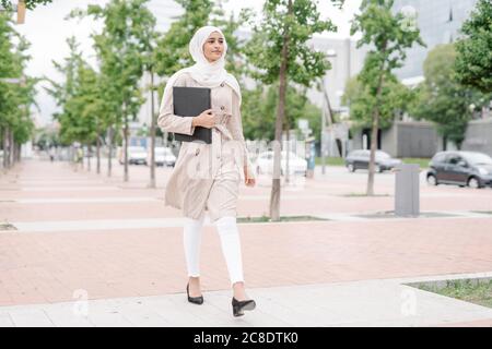 Jeune fille musulmane tenant une chemise tout en marchant sur le trottoir à l'intérieur ville Banque D'Images