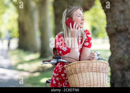 Femme attentionnés utilisant un smartphone tout en se penchant sur le vélo à parc public Banque D'Images