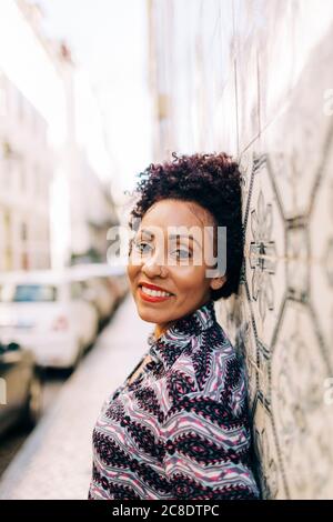 Femme élégante et souriante penchée sur un mur de carrelage en ville Banque D'Images