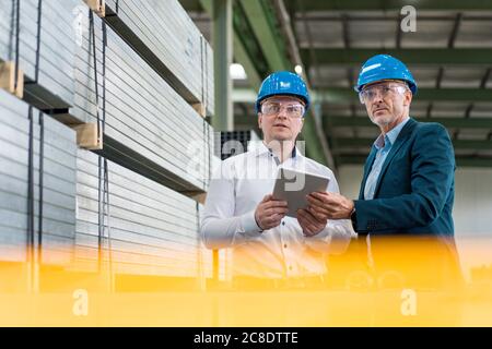 Deux hommes d'affaires portant des casques et des lunettes de sécurité dans un utilisation en usine de la tablette Banque D'Images