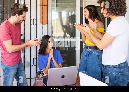 Des amis heureux applaudissant pour la belle jeune femme assise avec les mains classé à la cour arrière Banque D'Images