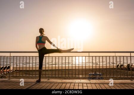 Femme sportive s'étendant sur le front de mer au lever du soleil, Gran Canaria, Espagne Banque D'Images