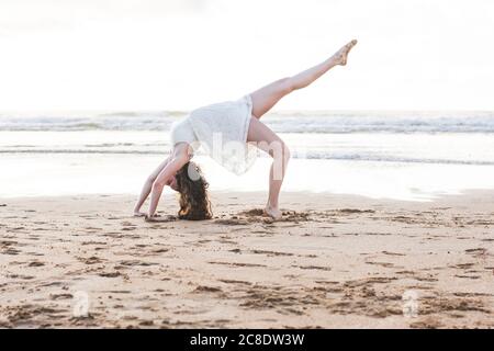 Jeune femme vêtue d'une robe blanche dansant sur le sable à la plage contre le ciel dégagé Banque D'Images