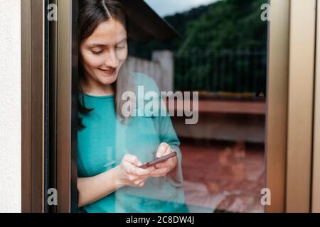 Femme utilisant un smartphone à la fenêtre, homme utilisant un ordinateur portable allongé sur le lit à la maison Banque D'Images