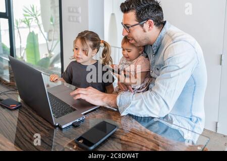 Homme de taille moyenne travaillant sur un ordinateur portable avec s'occuper de filles à la maison Banque D'Images