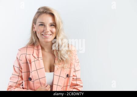 Femme blonde souriante avec une coiffure courbette vêtue d'une veste classique rose sur fond blanc. Banque D'Images