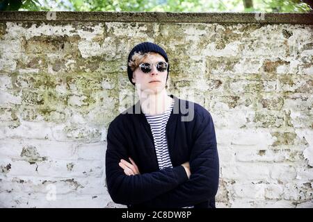 Portrait d'un jeune homme avec un casque portant des lunettes de soleil et un capuchon devant le mur abîmé Banque D'Images