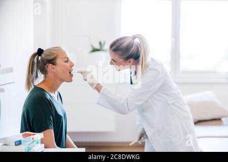 Femme médecin examinant une patiente avec un dépresseur de langue Banque D'Images