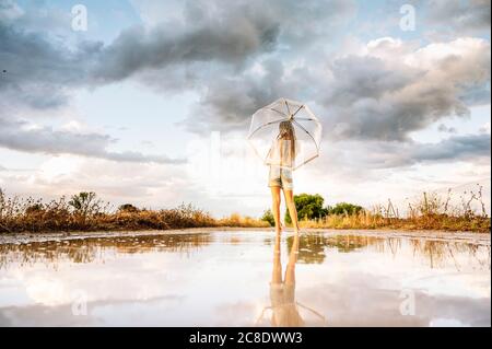 Pré-adolescente avec parapluie debout contre la réflexion sur la flaque Banque D'Images