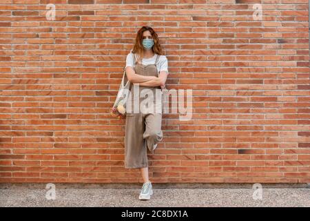 Jeune femme portant un masque avec les bras croisés s'appuyant sur la brique mur Banque D'Images