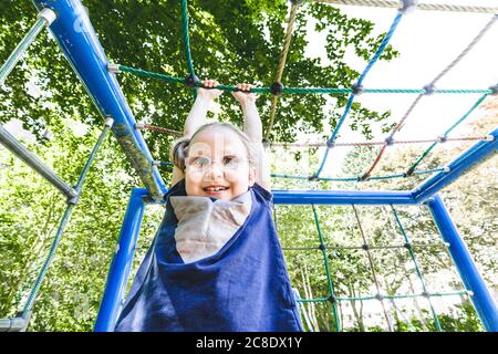 Jolie fille souriante accrochée à la jungle gym à l'aire de jeux dans stationnement Banque D'Images