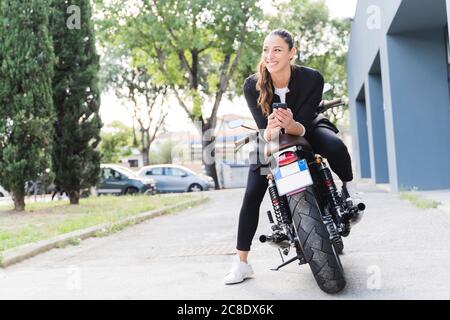 Femme souriante assise sur une moto et utilisant un smartphone Banque D'Images