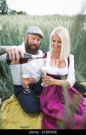 Homme versant du champagne dans un verre tenu par une femme pendant qu'elle est assise au milieu des plantes sur terre Banque D'Images