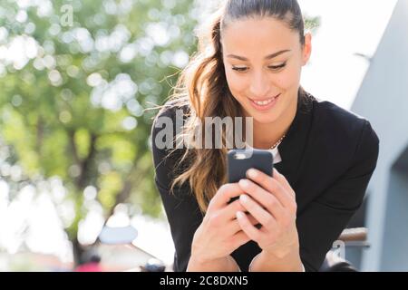 Femme souriante assise sur une moto et utilisant un smartphone Banque D'Images