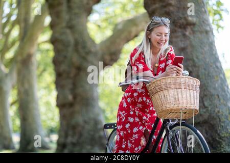 Femme joyeuse utilisant un smartphone tout en se penchant sur le vélo à parc public Banque D'Images