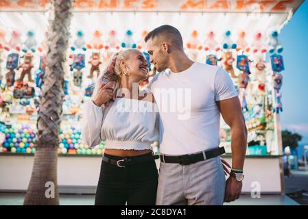 Homme romantique regardant une amie heureuse tout en se tenant contre la stalle au parc d'attractions Banque D'Images