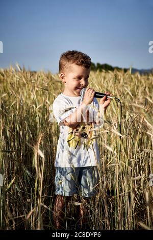 Garçon chantant au micro tout en se tenant au milieu des récoltes dans la ferme contre le ciel dégagé Banque D'Images