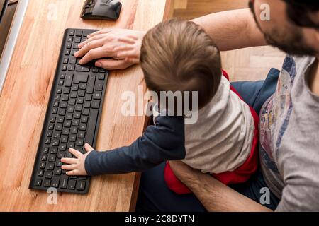 Père travaillant à la maison avec son bébé sur les genoux Banque D'Images