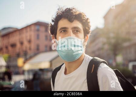 Gros plan d'un jeune homme attentif portant un masque de protection qui regarde loin en ville Banque D'Images