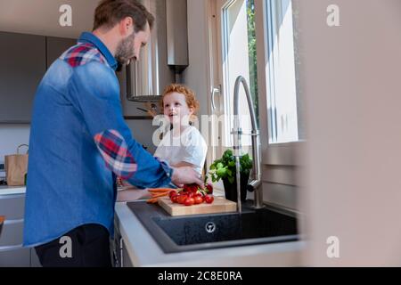 Adorable garçon regardant le père laver les tomates cerises dans la cuisine évier Banque D'Images