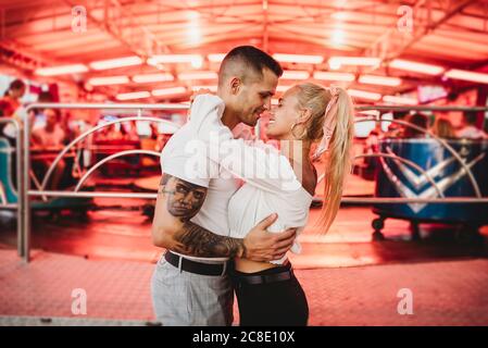 Un jeune couple romantique s'embrassant dans un parc d'attractions Banque D'Images