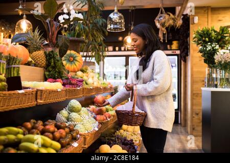 Jeune femme portant un panier en osier tout en achetant des fruits à l'épicerie stocker Banque D'Images