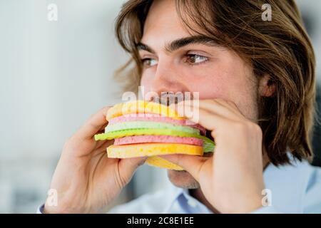 Gros plan sur un homme d'affaires qui regarde loin tout en mangeant un hamburger en éponge dans le café Banque D'Images