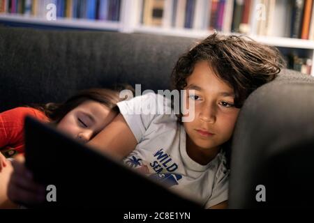 Fille dormant par frère en utilisant la tablette numérique tout en se relaxant canapé à la maison Banque D'Images