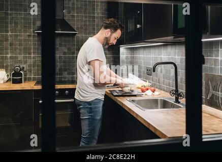 Homme mûr debout dans la cuisine, hacher des oignons Banque D'Images