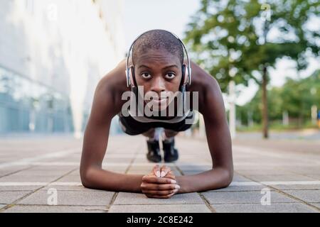 Femme assurée avec la tête rasée écouter de la musique tout en faisant des planches sur le sentier Banque D'Images