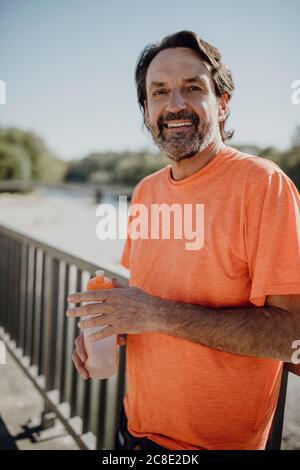 Portrait d'un homme souriant tenant une bouteille d'eau tout en se tenant contre ciel dégagé dans le parc Banque D'Images