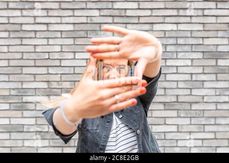 Gros plan de la femme adulte de taille moyenne faisant le cadre du doigt contre le gris mur de briques