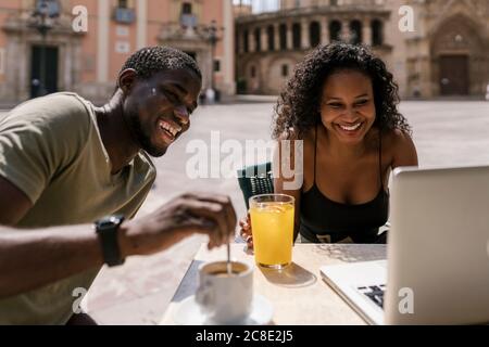 Un homme et une femme heureux utilisant un ordinateur portable au café-terrasse Banque D'Images