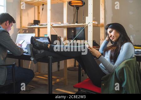 Femme détendue utilisant un smartphone au bureau et homme d'affaires utilisant un ordinateur portable Banque D'Images