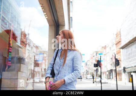 Jeune femme à tête rouge regardant par la fenêtre du magasin dans la ville Banque D'Images