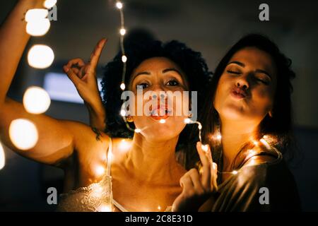 Gros plan d'amis féminins avec des guirlandes lumineuses qui s'amusent à accueil Banque D'Images