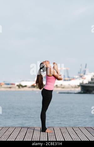 Athlète féminine avec les yeux fermés méditant en se tenant debout sur la jetée contre la mer Banque D'Images