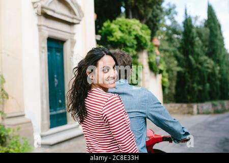 Femme souriante assise avec un petit ami sur Vespa Banque D'Images