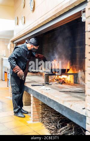 Cuisine traditionnelle de paella dans la cuisine du restaurant, chef portant un masque de protection Banque D'Images