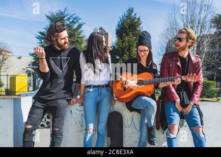 Femme adulte de taille moyenne jouant de la guitare tout en appréciant avec des amis ville Banque D'Images