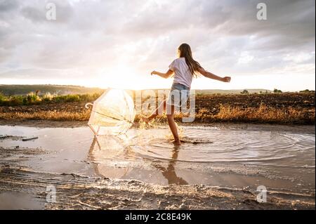 Une fille éclabousse de l'eau sur un parasol au coucher du soleil Banque D'Images