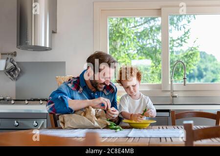 Homme souriant regardant le fils tenant le pois dans la cuisine Banque D'Images