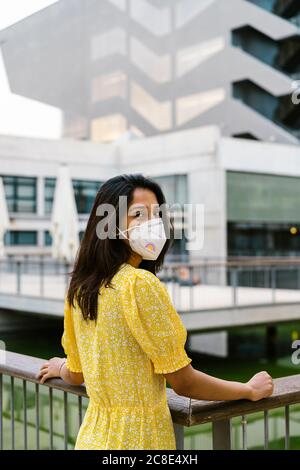 Jeune femme portant un masque facial sur une passerelle surélevée en ville Banque D'Images