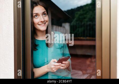 Femme utilisant un smartphone à la fenêtre, homme utilisant un ordinateur portable allongé sur le lit à la maison Banque D'Images