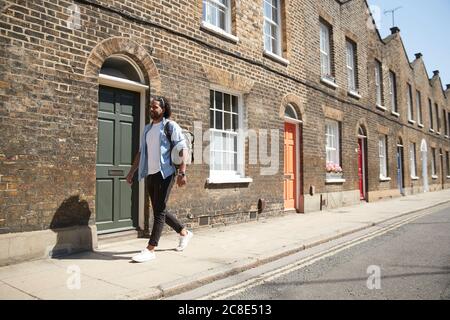 Jeune homme marchant sur la chaussée devant les maisons résidentielles, Londres, Royaume-Uni Banque D'Images