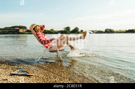 Jeune femme assise sur une chaise longue dans les éclaboussures avec de l'eau de la rivière Banque D'Images