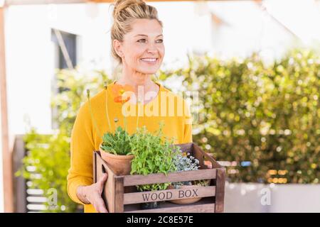Portrait de la femme mûre heureuse avec boîte de plantes en bois sur la terrasse Banque D'Images
